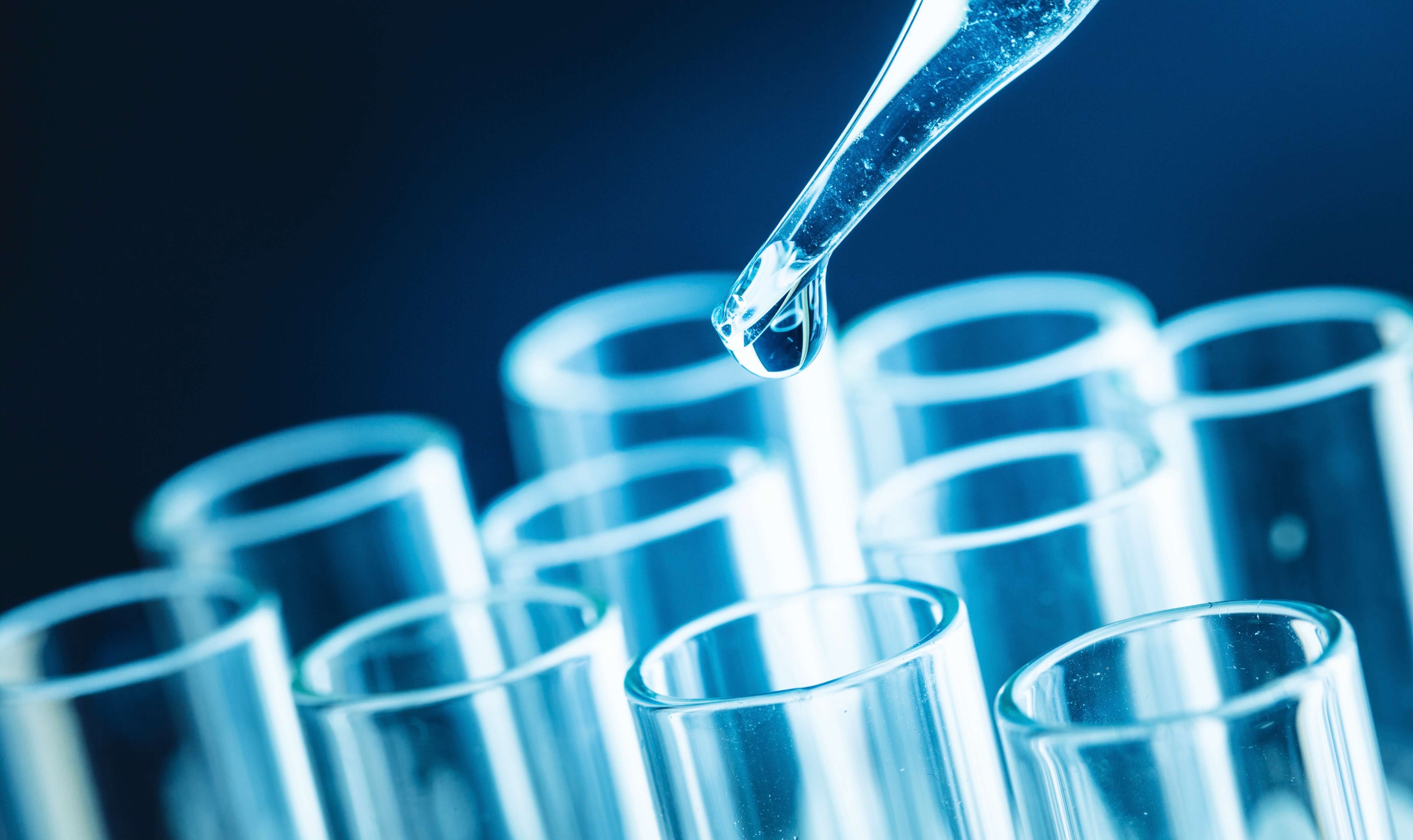 A pipette drips clear liquid into test tubes