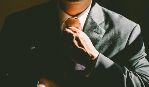 A man in a black suit loosening his tie